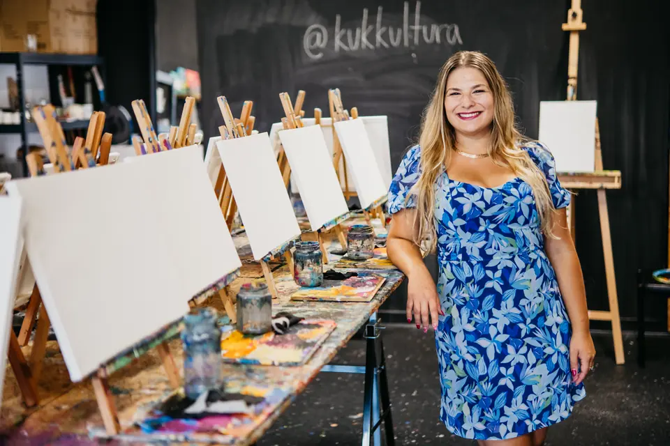 Bianca v modrých šatách pred radom prázdnych plátien a tabuľou @kukkultura