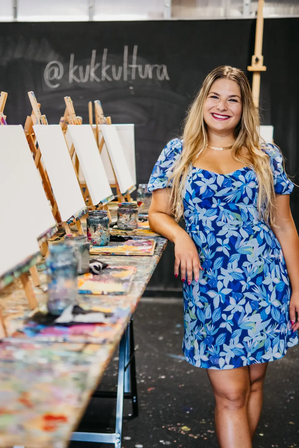Bianca Andrašková Macková v modrých šatách opretá o stôl v ateliéri